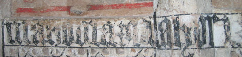 Detalle de pintura mural dañada con inscripción gótica en negro y banda roja sobre enlucido envejecido.