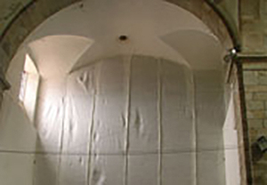 Interior de iglesia con bóveda de arista y arco de piedra; cerramiento temporal de plástico blanco cubre el ábside.